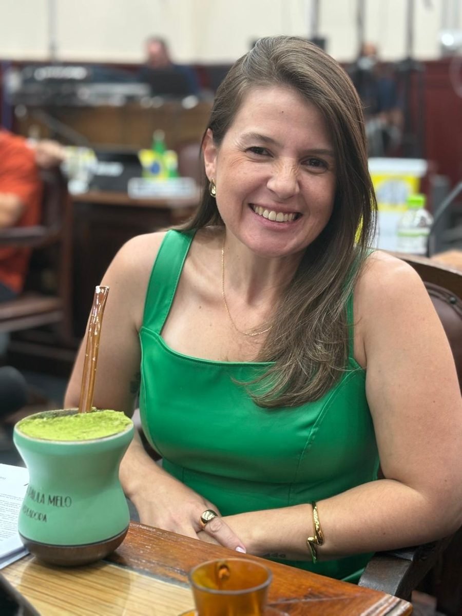 Ana Paula Melo sorri em sua bancada no plenário, ao lado de uma cuia de chimarrão com seu nome